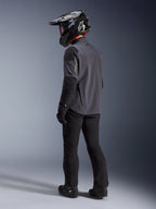 Motociclista de aventura con la chaqueta Maxdura Drystar®XF Laminada con Armadura en Deep Gray Black, vista posterior. Equipamiento completo con pantalones de moto negros, casco de motocross negro con marca Alpinestars y botas off-road negras. Conjunto técnico para todo clima para rendimiento dual-sport.