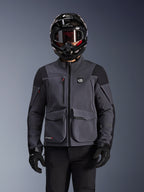 Alpinestars Maxdura Drystar®XF Laminated Armored Shell, chaqueta de motocicleta en gris oscuro y negro, usada por un piloto con casco negro, gafas y guantes, con grandes bolsillos técnicos tipo cargo y marca ALL TERRA, equipamiento de aventura touring
