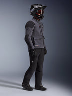 Motociclista con chaqueta Alpinestars Maxdura Drystar®XF Laminated Armored Shell en gris oscuro y negro, combinada con pantalones de aventura negros, casco negro con gafas, guantes y botas negros, toma de estudio de cuerpo completo que destaca el equipamiento técnico dual-sport.