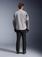 Alpinestars Maxdura Drystar®XF Laminated Armored Shell, chaqueta de motociclismo en gris medio y gris oscuro, vista trasera, con un cuerpo gris claro, paneles gris oscuro en los hombros y las mangas, un pequeño logotipo de la estrella Alpinestars en rojo en la parte posterior del cuello y marca blanca en la manga izquierda, combinada con pantalones y botas de montar negros.