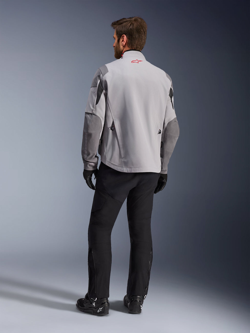 Maxdura Drystar®XF Laminated Armored Shell, chaqueta de moto, gris medio y gris oscuro, vista trasera con el logo rojo de Alpinestars en el cuello, refuerzos gris oscuro en las mangas, usada con pantalones y botas negros, equipamiento para conducción de aventura