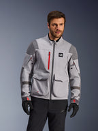 Alpinestars Maxdura Drystar®XF Laminated Armored Shell, chaqueta de motociclismo de aventura, gris medio y gris oscuro con detalles en rojo, vestida por un modelo con guantes y pantalones negros, con grandes bolsillos de carga y cremalleras impermeables, equipamiento profesional para conducción