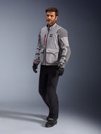 Alpinestars Maxdura Drystar®XF Laminated Armored Shell, chaqueta de motociclismo de aventura, gris medio y gris oscuro, lucida por un modelo con pantalones y guantes de conducción negros, con acentos de cremallera en rojo y bolsillos de carga, equipo técnico profesional para todo clima diseñado para adventure touring.