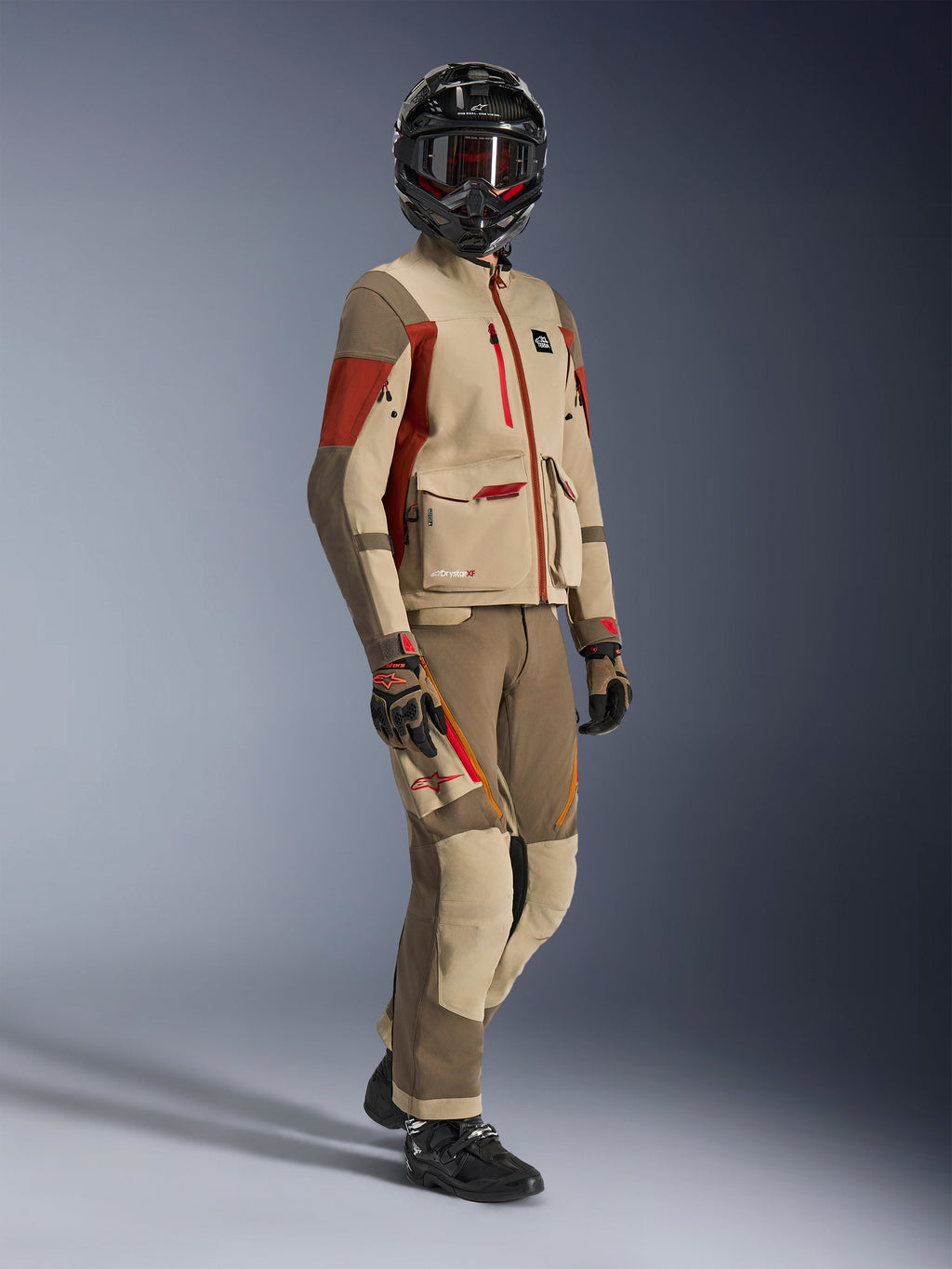 Piloto de aventura vistiendo la chaqueta Maxdura Drystar®XF Laminated Armored Shell en color Aluminum Walnut y Rust Brown con pantalones a juego en nogal y canela, casco negro de fibra de carbono y botas de moto negras, equipamiento técnico de touring para motociclismo de aventura