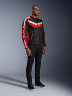 Modelo masculino vistiendo la chaqueta Alpinestars T-Dyno WR, chaqueta de moto textil en negro, rojo brillante y crudo, con rayas rojas y blanco roto y logotipos de estrella de Alpinestars en las mangas, combinada con pantalones negros y zapatillas altas negras, equipamiento de conducción urbana de inspiración vintage.