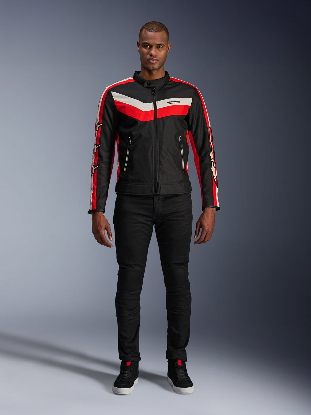 Chaqueta Alpinestars T-Dyno WR, chaqueta de moto textil en negro, rojo brillante y crudo, con franjas en forma de V en el pecho y logotipos de estrellas en las mangas, combinada con pantalones negros y calzado de moto negro, equipamiento urbano de inspiración heritage