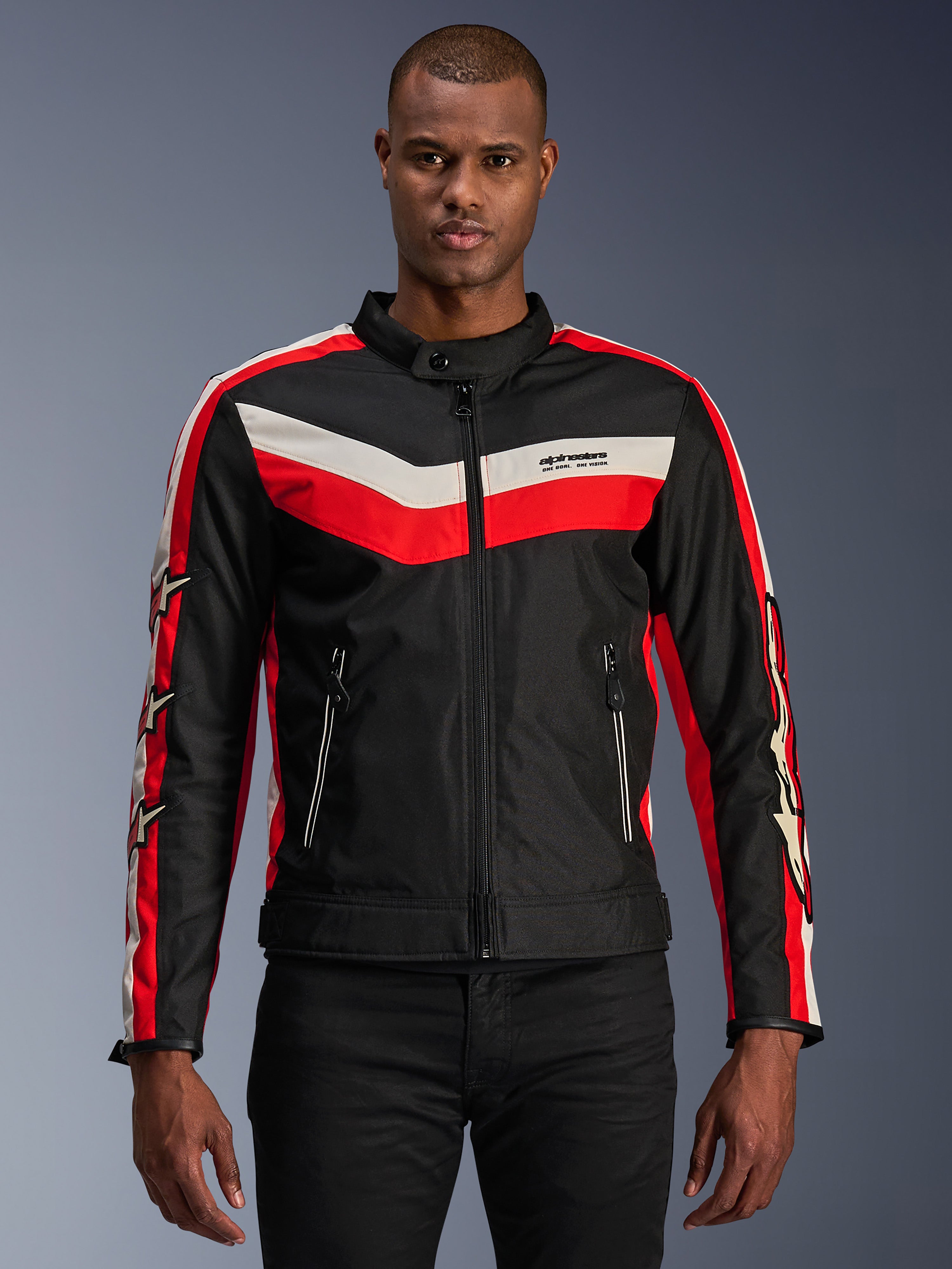 Chaqueta Alpinestars T-Dyno WR, chaqueta textil de moto, negra con franjas tipo chevrón en rojo brillante y crudo, ajuste de motociclista de inspiración vintage, cuello alto con cierre de botón, bolsillos frontales con cremallera, logotipos de estrellas en las mangas, usada por modelo