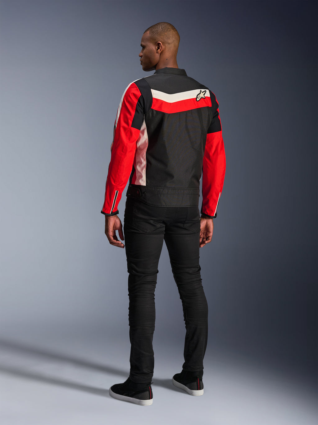 Chaqueta Alpinestars T-Dyno WR, chaqueta textil de moto, negro, rojo brillante y crudo, vista posterior en modelo, ajuste de motociclista de inspiración vintage con paneles de colores clásicos y logotipo, equipamiento urbano moderno para carretera.
