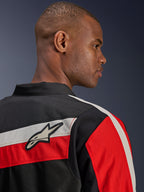 Chaqueta Alpinestars T-Dyno WR, vista de cerca de la parte posterior en un modelo, chaqueta textil de moto en color negro con franjas horizontales en color crudo y rojo brillante, con el parche del logotipo de la estrella de Alpinestars en el hombro, estilo biker de inspiración clásica