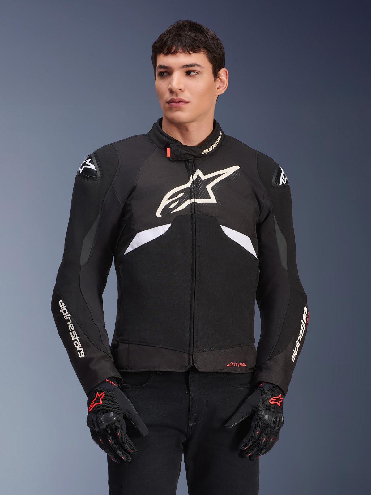 Alpinestars T-GP R V3 Drystar Jacket, chaqueta textil deportiva impermeable, negra y blanca con acentos rojos, con un gran logo de estrella blanca en el pecho y marca blanca en las mangas, usada con guantes de moto negros y rojos
