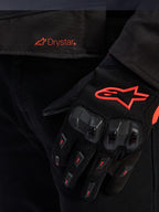 Primer plano de la cintura de la chaqueta Alpinestars T-GP R V3 Drystar® con el logotipo Drystar en rojo, mostrada con un guante de moto negro con el logotipo de la estrella de Alpinestars en rojo, tejido de malla y protección de nudillos reforzada.