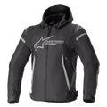 Alpinestars Zaca Waterproof Jacket, chaqueta deportiva para moto, negro y gris oscuro, con capucha desmontable, logotipo grande gris en el pecho, detalles en gris claro en los hombros y laterales, correas de ajuste en la cintura y cierre frontal de cremallera, confección textil deportiva