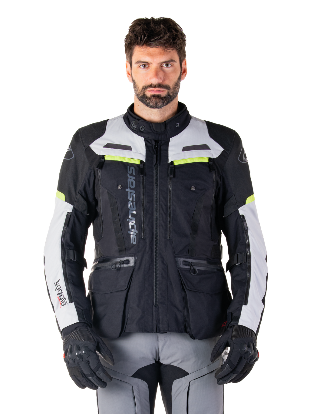 Hombre con la chaqueta Alpinestars Bogotá Pro Drystar®, en colores negro, gris hielo y amarillo flúor, una chaqueta de moto touring de aventura para todas las estaciones, con diseño impermeable, múltiples bolsillos y logotipo vertical, combinada con guantes negros y pantalones de motorista grises