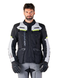 Hombre con la chaqueta Alpinestars Bogotá Pro Drystar®, en colores negro, gris hielo y amarillo flúor, una chaqueta de moto touring de aventura para todas las estaciones, con diseño impermeable, múltiples bolsillos y logotipo vertical, combinada con guantes negros y pantalones de motorista grises
