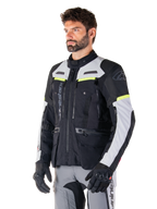 Chaqueta Alpinestars Bogotá Pro Drystar®, chaqueta de moto adventure touring, negro, gris hielo y amarillo flúor, vestida por un hombre con pantalones grises a juego y guantes negros, con paneles de ventilación técnica y diseño multibolsillos.