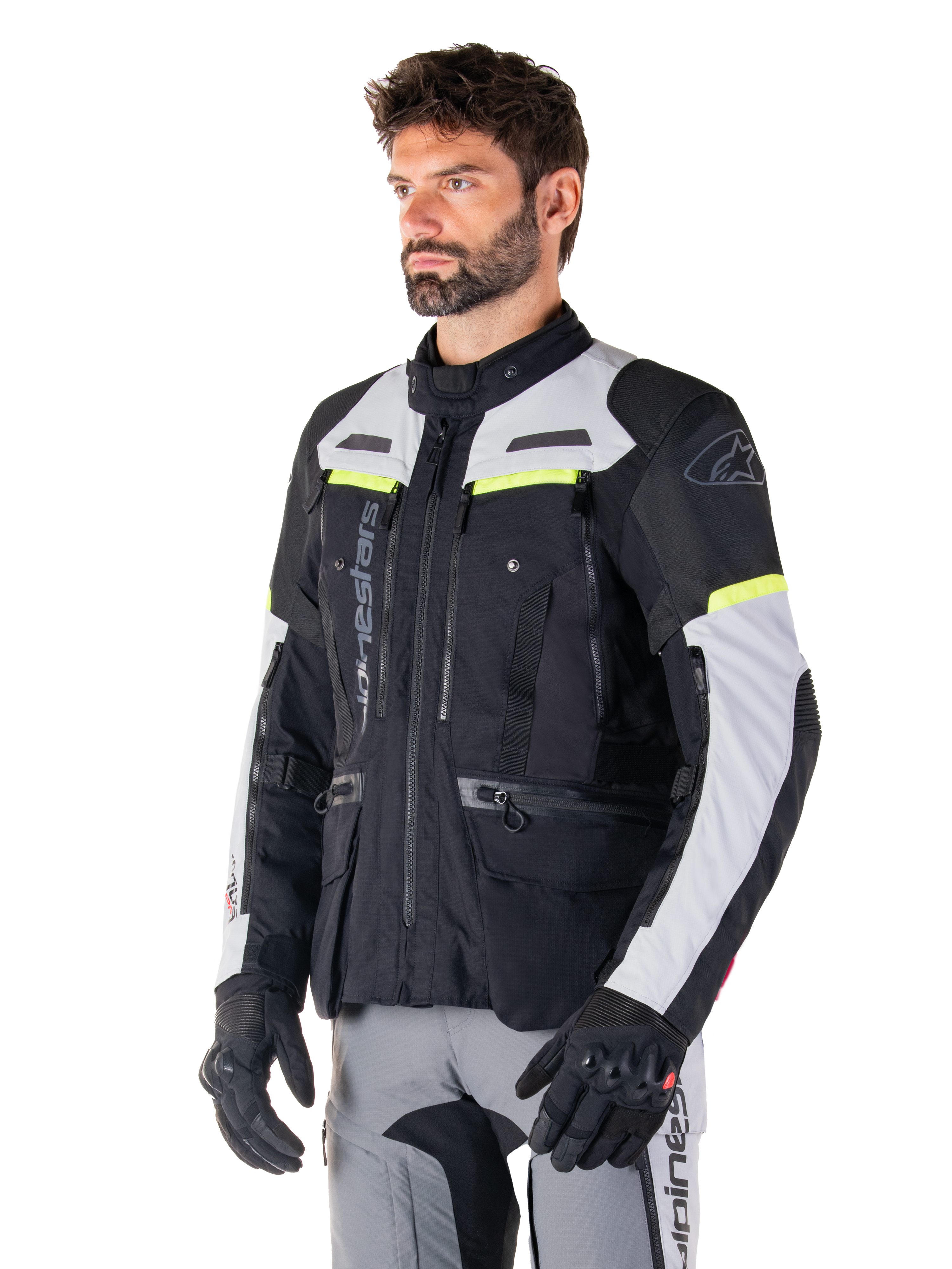 Chaqueta Alpinestars Bogotá Pro Drystar®, chaqueta de moto adventure touring, negro, gris hielo y amarillo flúor, vestida por un hombre con pantalones grises a juego y guantes negros, con paneles de ventilación técnica y diseño multibolsillos.