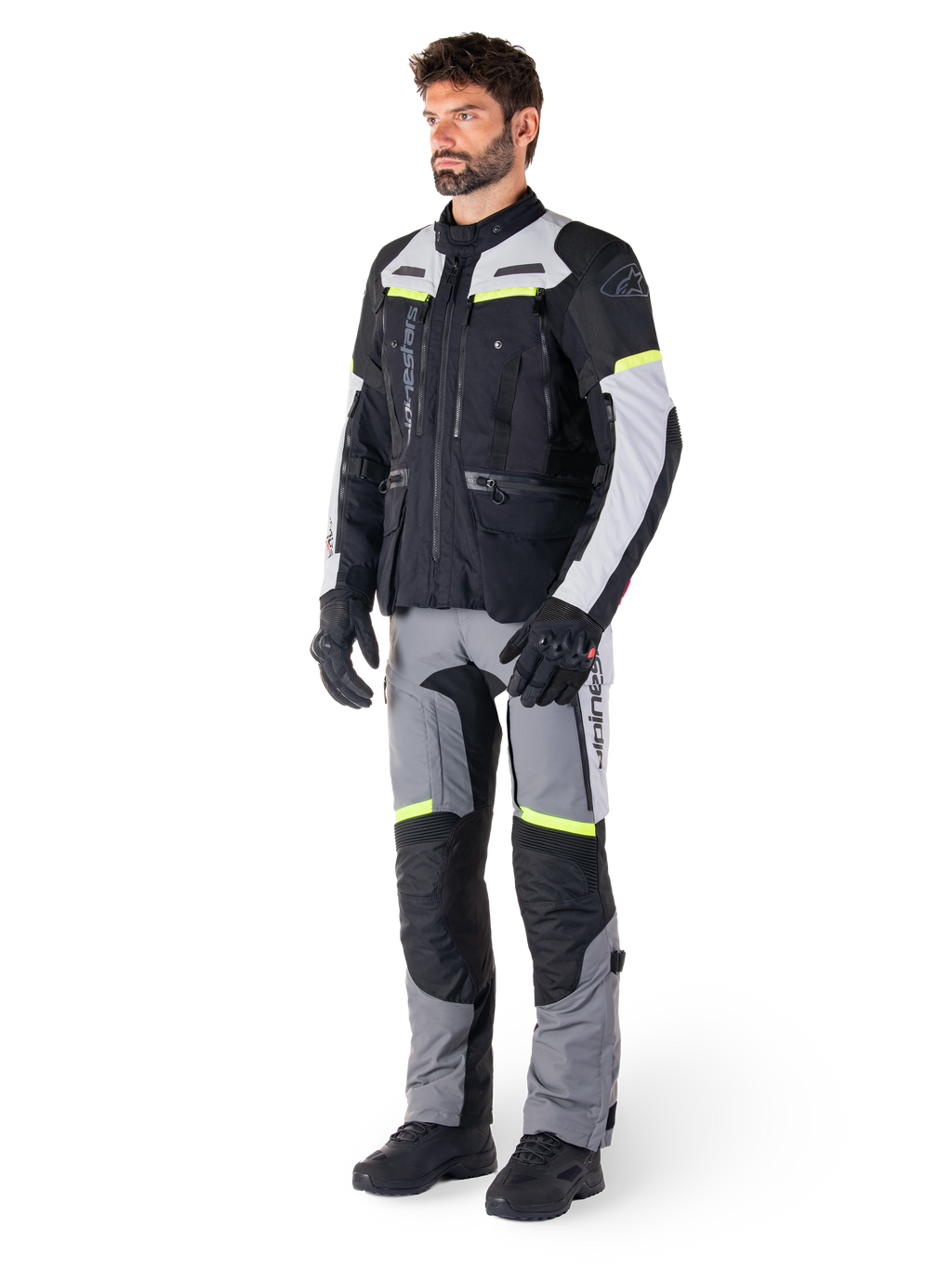 Chaqueta Alpinestars Bogotá Pro Drystar®, chaqueta de moto adventure touring, Negro Gris Hielo Amarillo Flúor, usada por un modelo con pantalones a juego y guantes negros, con confección textil impermeable, paneles de ventilación y detalles fluorescentes.
