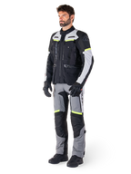 Chaqueta Alpinestars Bogotá Pro Drystar®, chaqueta de moto adventure touring, Negro Gris Hielo Amarillo Flúor, usada por un modelo con pantalones a juego y guantes negros, con confección textil impermeable, paneles de ventilación y detalles fluorescentes.