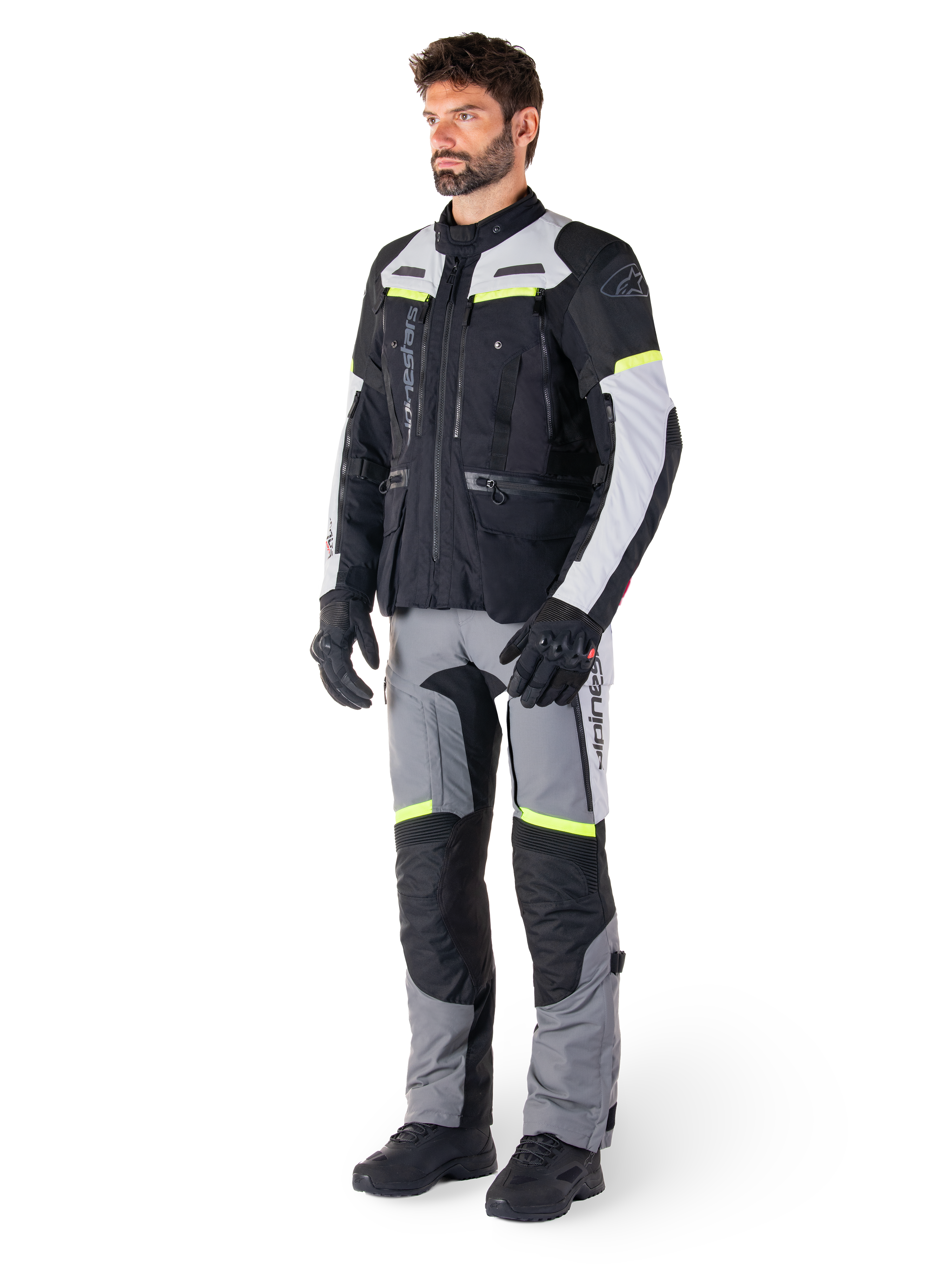Chaqueta Alpinestars Bogotá Pro Drystar®, chaqueta de moto adventure touring, Negro Gris Hielo Amarillo Flúor, usada por un modelo con pantalones a juego y guantes negros, con confección textil impermeable, paneles de ventilación y detalles fluorescentes.