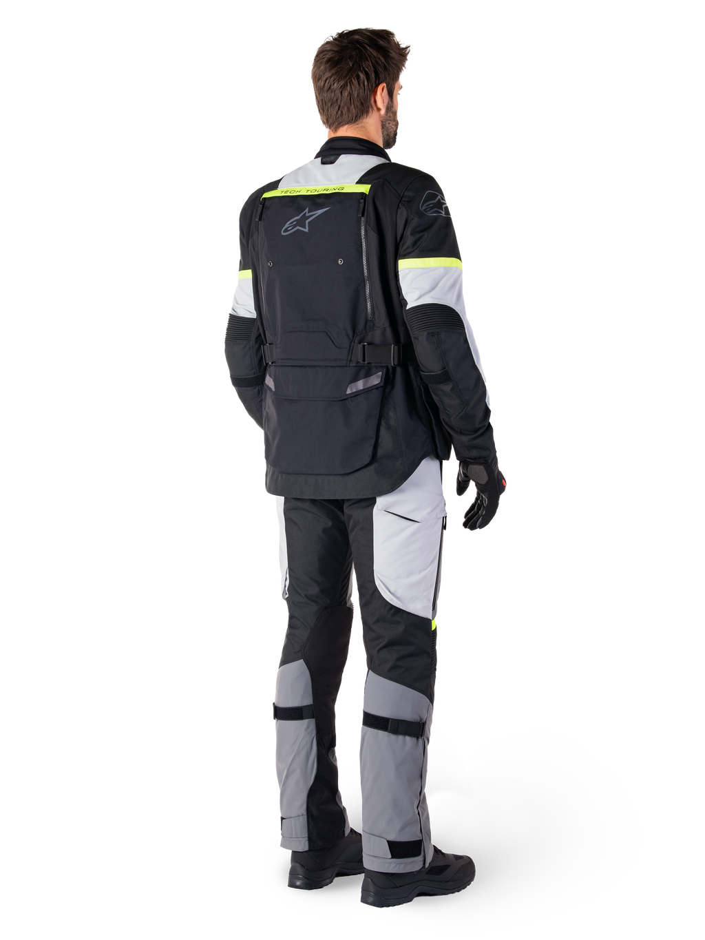 Vista trasera de un piloto con la chaqueta Alpinestars Bogotá Pro Drystar® en color Black Ice Gray Yellow Fluo, combinada con pantalones de adventure touring a juego, con un gran bolsillo trasero y detalles en amarillo flúor, equipamiento textil de moto para todas las estaciones.