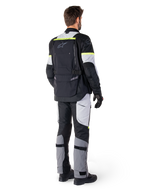 Vista trasera de un piloto con la chaqueta Alpinestars Bogotá Pro Drystar® en color Black Ice Gray Yellow Fluo, combinada con pantalones de adventure touring a juego, con un gran bolsillo trasero y detalles en amarillo flúor, equipamiento textil de moto para todas las estaciones.