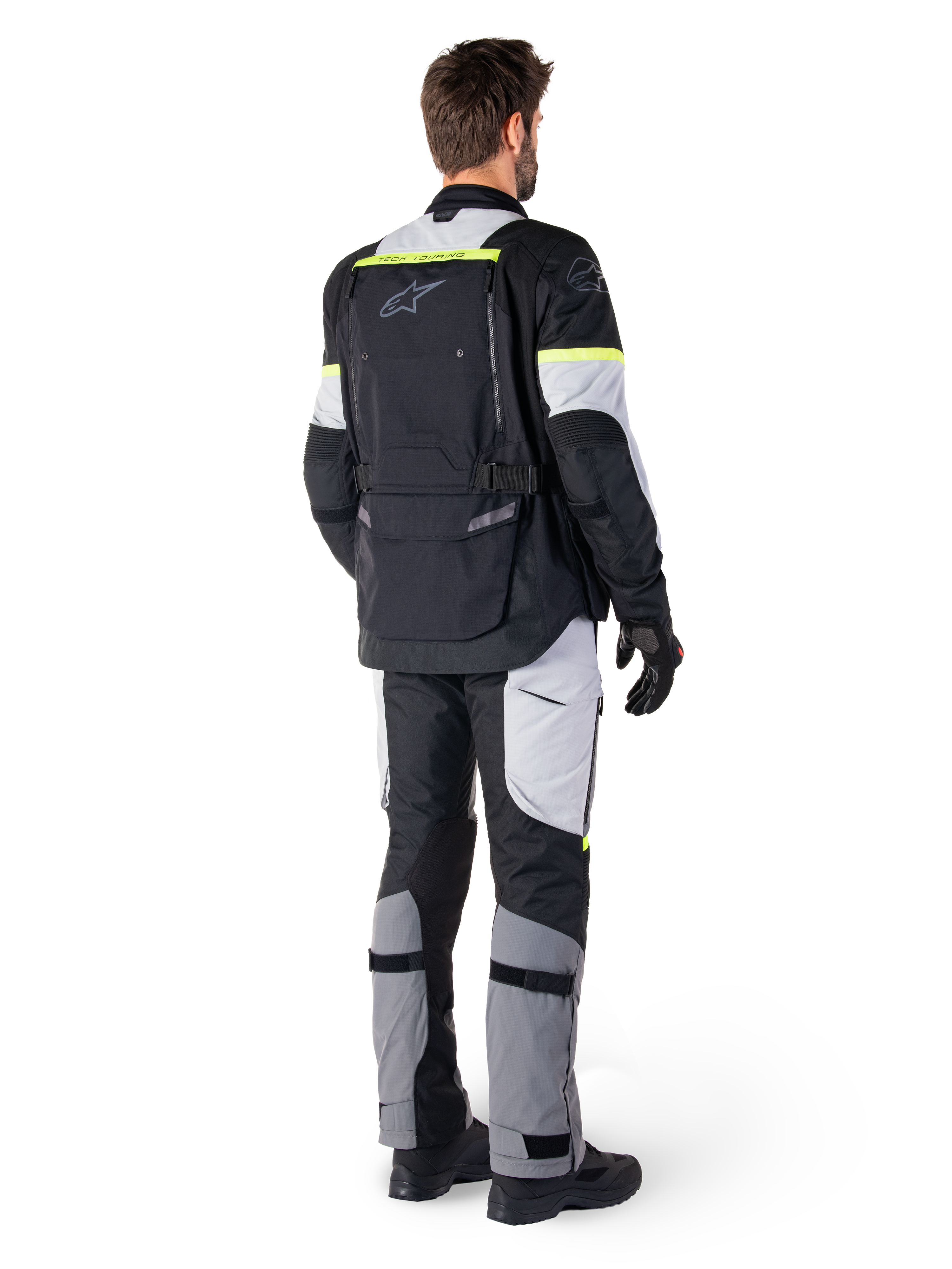 Vista trasera de un piloto con la chaqueta Alpinestars Bogotá Pro Drystar® en color Black Ice Gray Yellow Fluo, combinada con pantalones de adventure touring a juego, con un gran bolsillo trasero y detalles en amarillo flúor, equipamiento textil de moto para todas las estaciones.