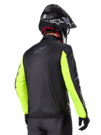 Chaqueta Alpinestars Bogotá Pro Drystar®, vista trasera, negra con mangas en amarillo flúor, usada por un piloto con casco y guantes negros, equipamiento de moto de alta visibilidad para adventure touring con acabado textil técnico.