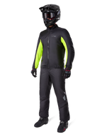 Motociclista vistiendo el forro de la chaqueta Alpinestars Bogotá Pro Drystar®, negro con paneles amarillo flúor brillantes en las mangas, combinado con pantalones negros a juego, casco de motocross y guantes negros, equipamiento de aventura impermeable para todas las estaciones