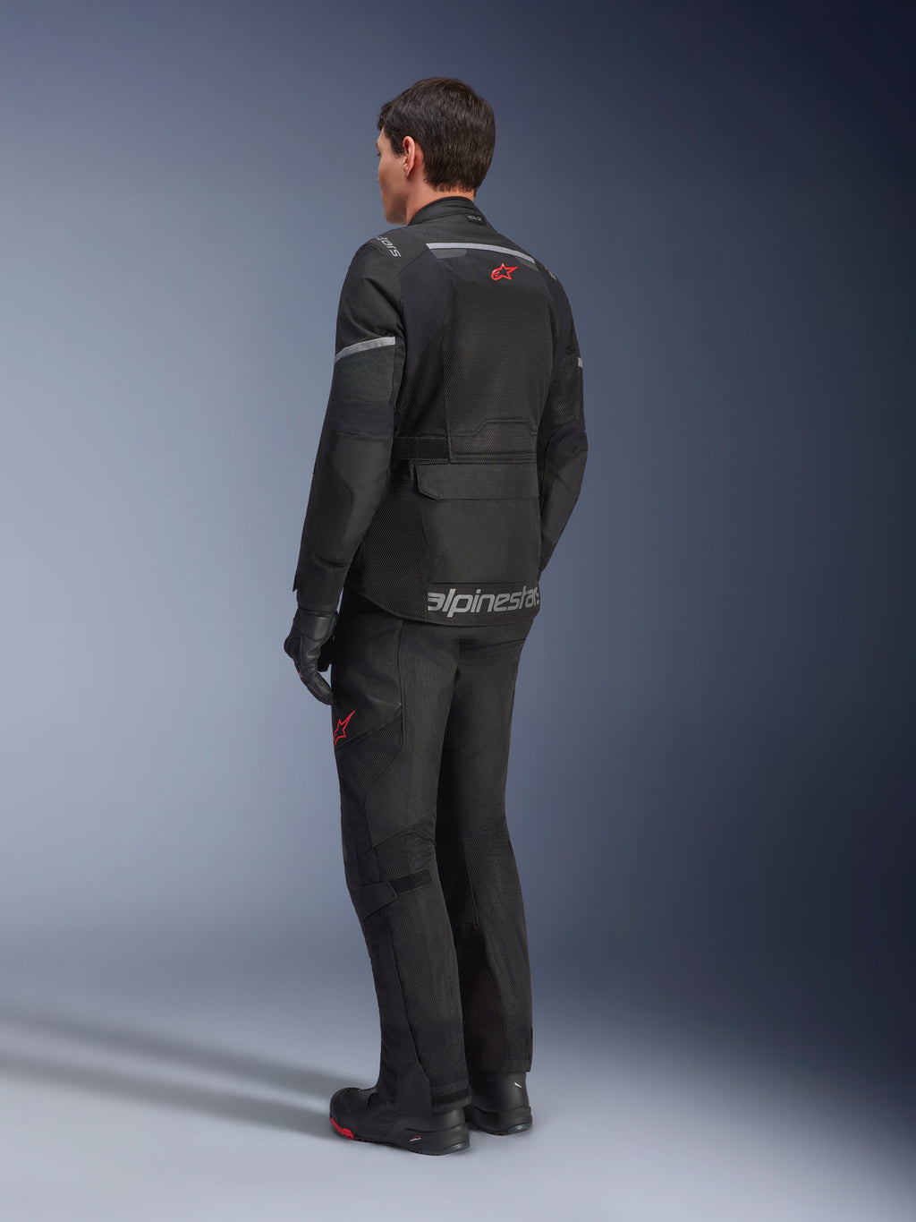 Pantalones Alpinestars Andes Air Drystar® y chaqueta a juego, negros con logotipos de estrella rojos, equipamiento de moto para aventura touring visto desde atrás, con paneles de ventilación de malla y detalles reflectantes.