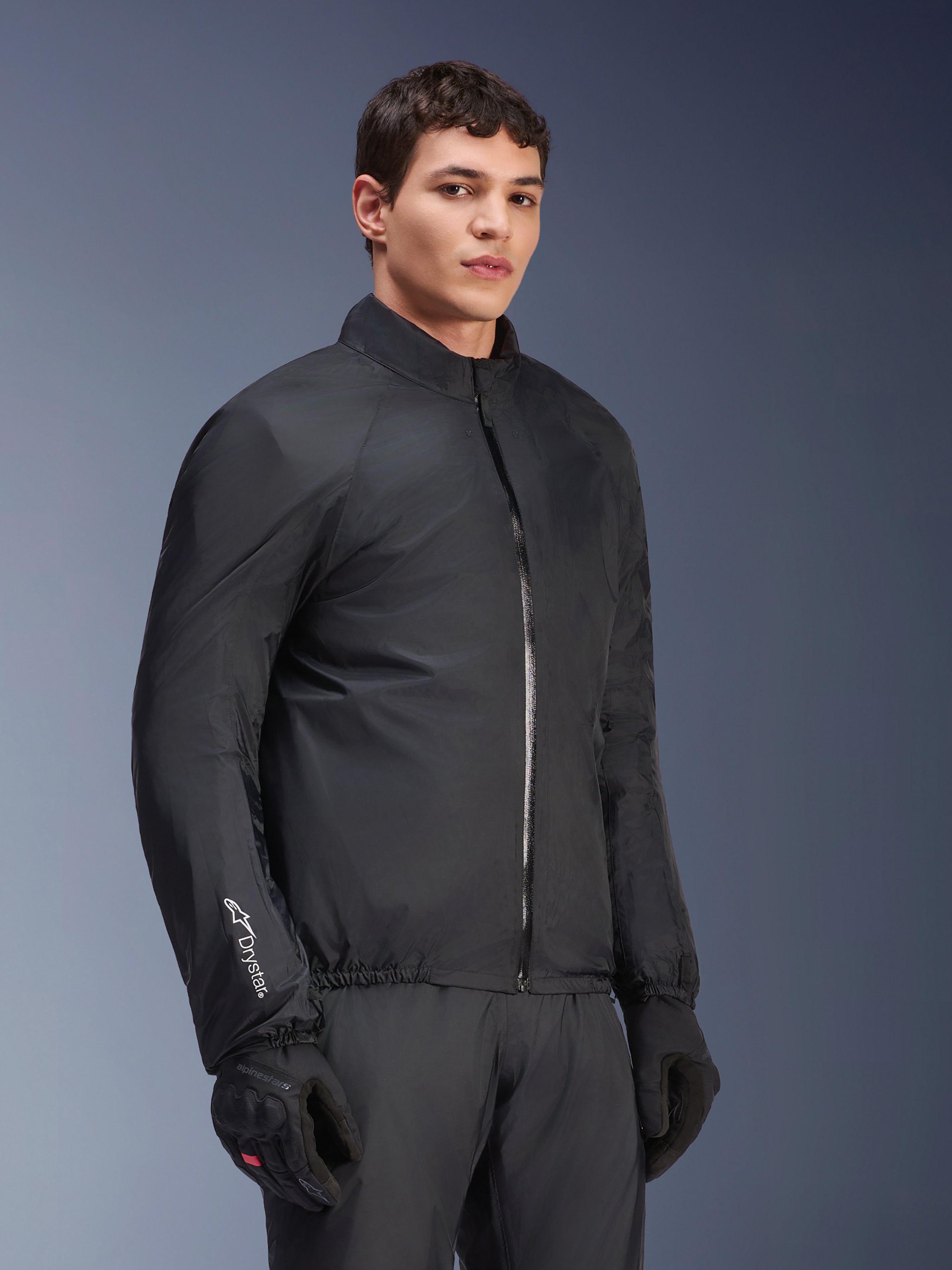 Membrana impermeable de la chaqueta Alpinestars Andes Air Drystar®, negra, usada por un modelo masculino con guantes y pantalones negros, textil técnico ligero con la marca 'Drystar' en la manga, toma de estudio