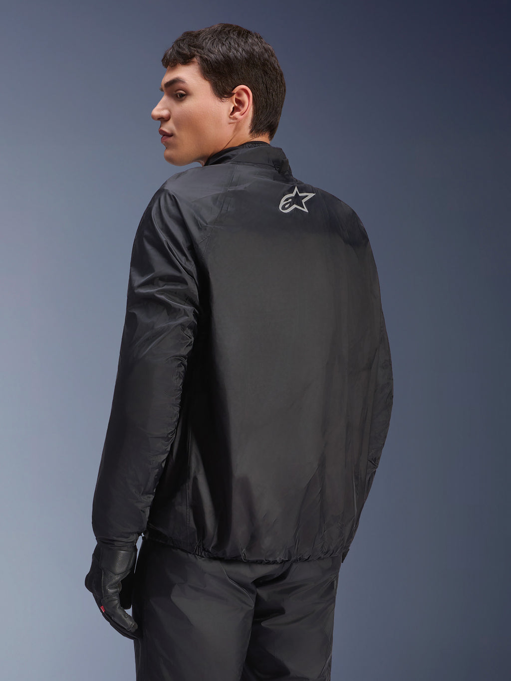 Chaqueta Alpinestars Andes Air Drystar®, membrana impermeable desmontable en negro, vista posterior en un modelo masculino, con un pequeño logotipo blanco de Alpinestars en la parte superior de la espalda, combinada con guantes de conducción negros