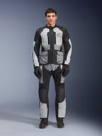 Chaqueta Alpinestars Andes Air Drystar® en gris hielo, gris oscuro y negro, usada por un modelo masculino con pantalones de motociclismo y guantes a juego, diseño de turismo de aventura con grandes bolsillos frontales y detalles en amarillo fluorescente, vista frontal de estudio