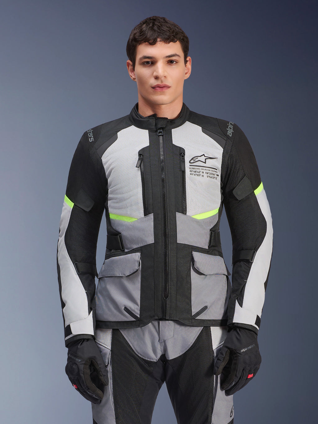 Piloto con chaqueta Alpinestars Andes Air Drystar® en gris hielo, gris oscuro y negro, con detalles en amarillo neón y paneles de ventilación de malla, combinada con pantalones y guantes de moto a juego, equipamiento de adventure touring