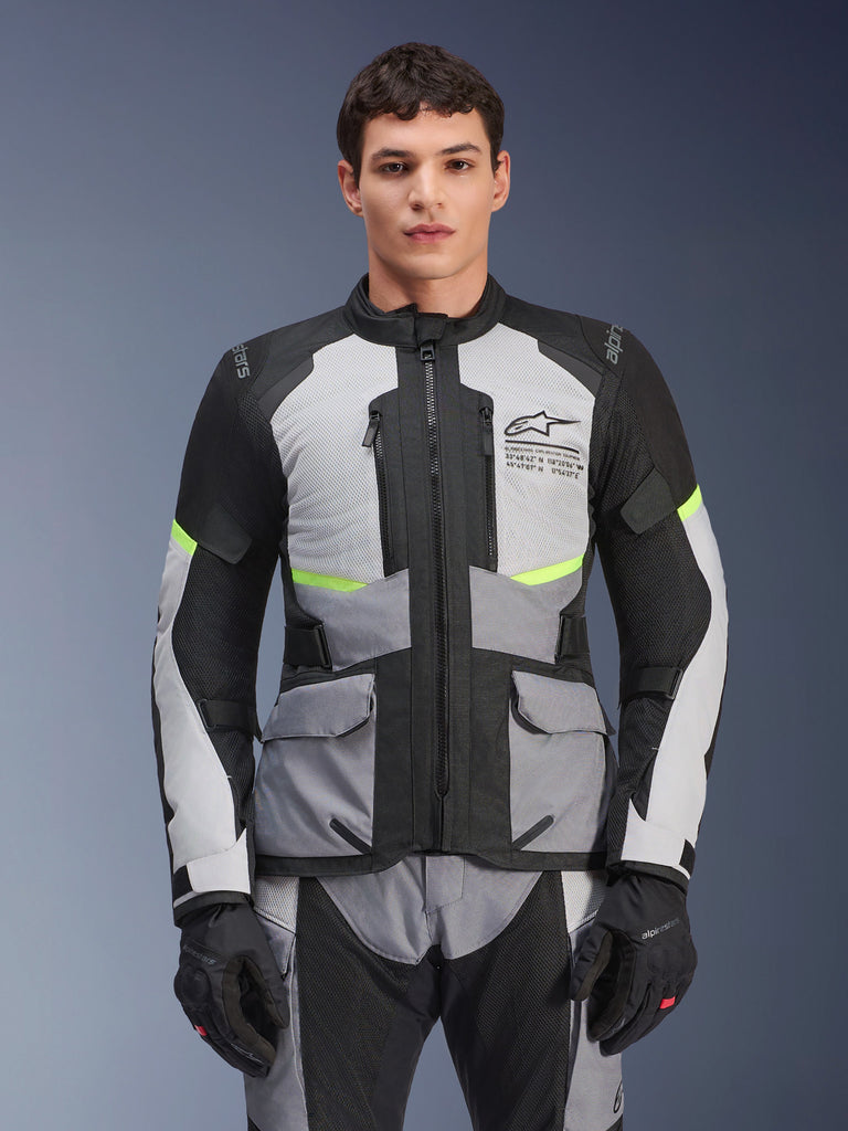 Piloto con chaqueta Alpinestars Andes Air Drystar® en gris hielo, gris oscuro y negro, con detalles en amarillo neón y paneles de ventilación de malla, combinada con pantalones y guantes de moto a juego, equipamiento de adventure touring