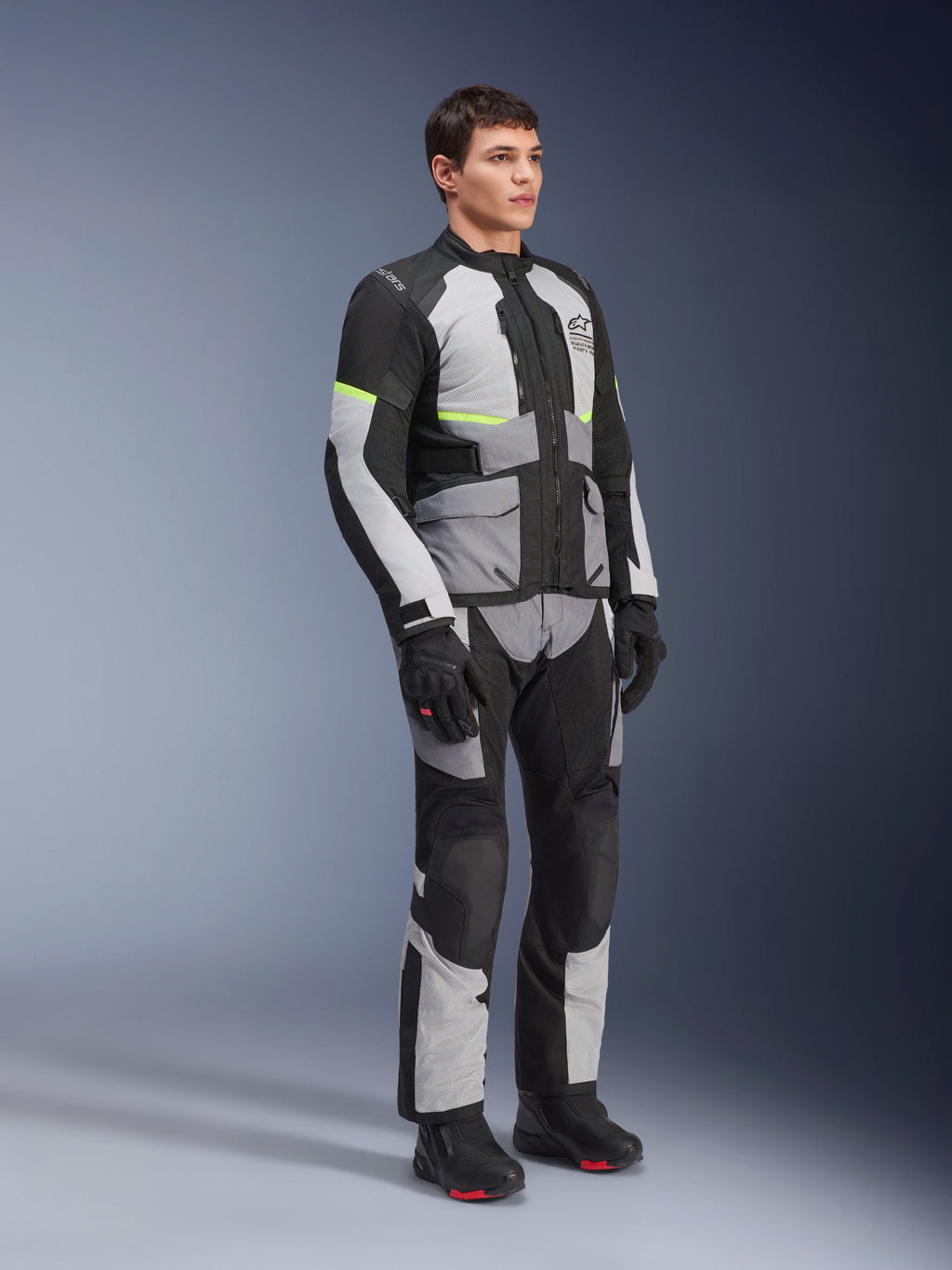 Chaqueta y pantalones Alpinestars Andes Air Drystar®, equipamiento de moto Adventure Touring, gris hielo, gris oscuro y negro con detalles en amarillo neón, combinados con guantes y botas negras, toma de estudio de cuerpo completo para turismo de dos estaciones