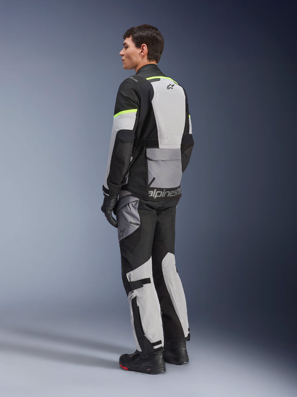 Piloto con chaqueta y pantalones Alpinestars Andes Air Drystar®, equipamiento adventure touring en color Ice Gray Dark Gray Black con detalles en amarillo neón, con amplios paneles de malla para el flujo de aire, logotipo de Alpinestars en la espalda, usado con guantes y botas negros.