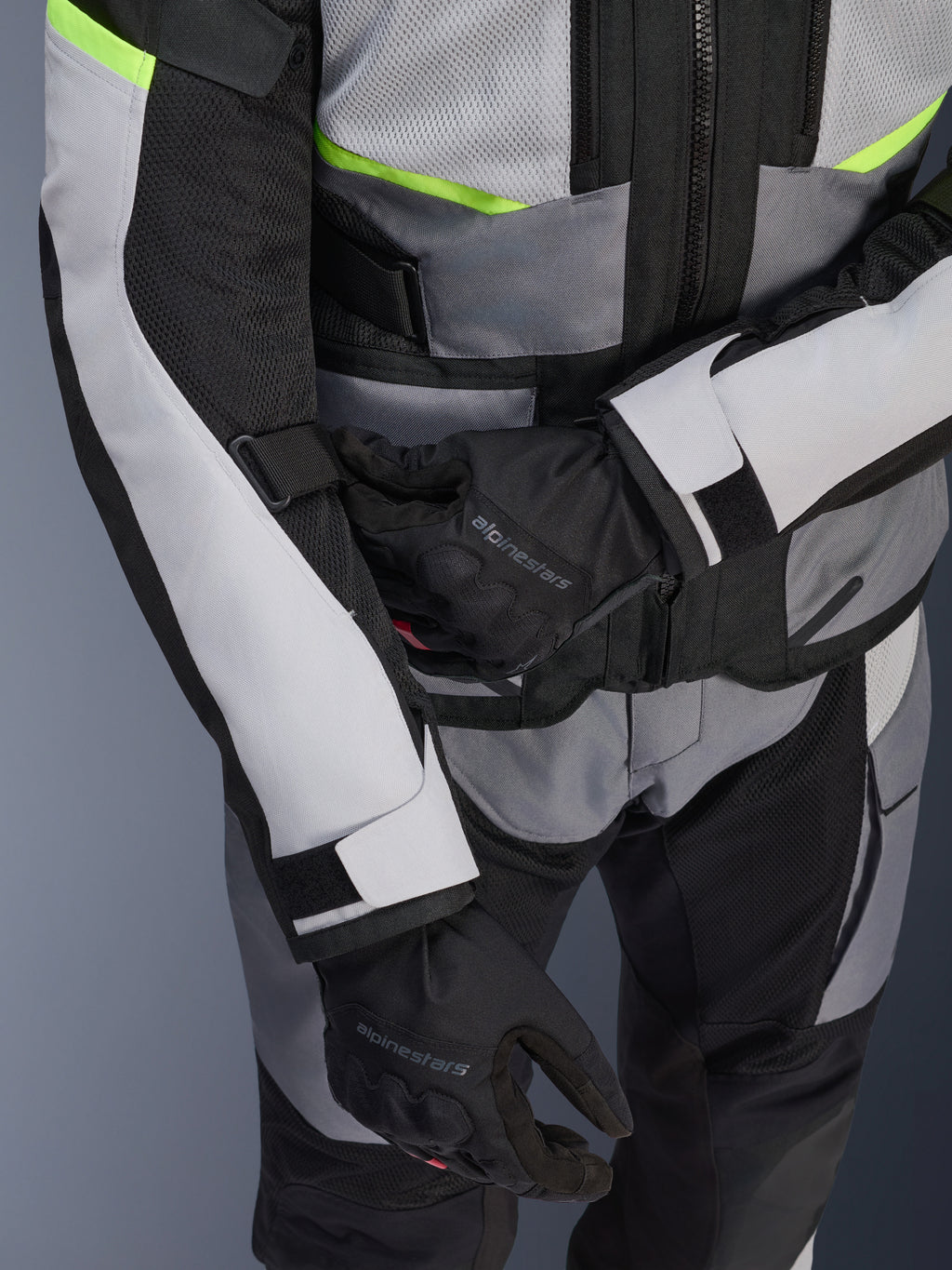 Chaqueta Alpinestars Andes Air Drystar®, chaqueta de moto touring, gris hielo y gris oscuro con detalles en amarillo neón, primer plano que muestra los paneles de malla y las correas de ajuste, usada con guantes negros Alpinestars