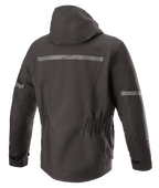 Chaqueta Alpinestars Sirius Drystar® Techshell, chaqueta de moto, Negro Melange, vista posterior con capucha integrada, franja reflectante con el logotipo de Alpinestars, cintura elástica y parte trasera alargada para mayor cobertura al conducir.