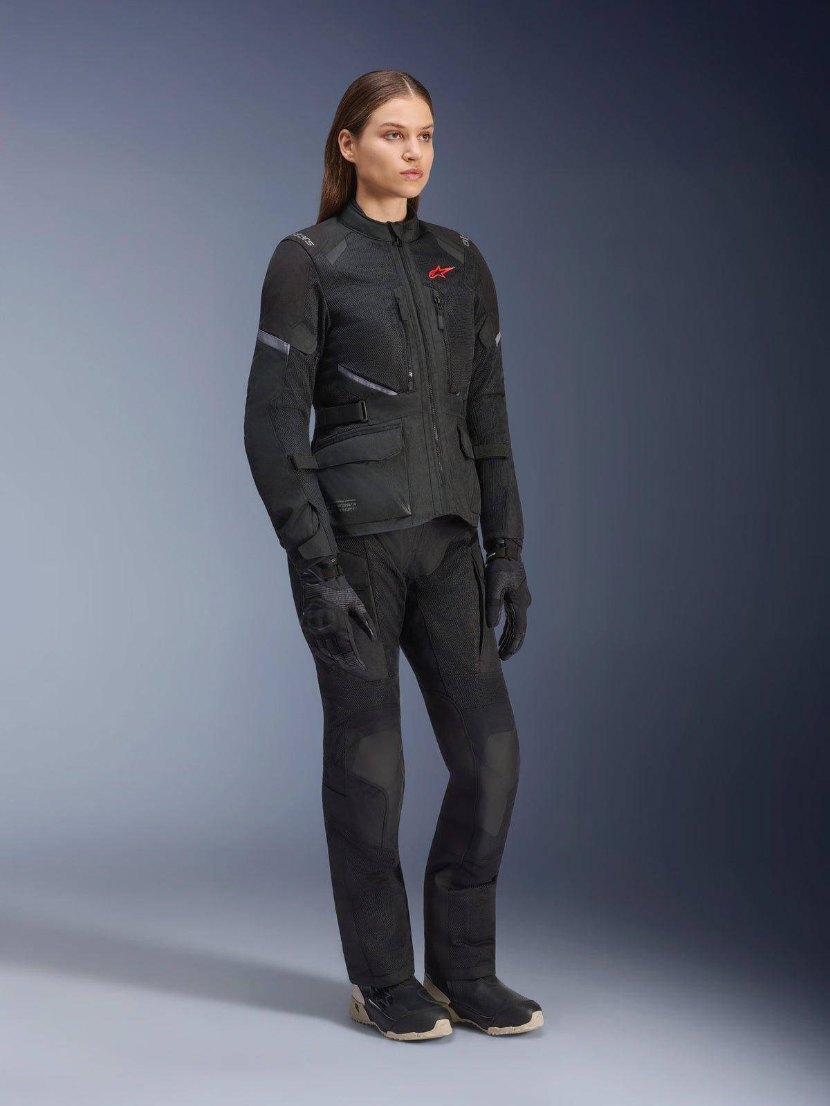 Mujer vistiendo la chaqueta Alpinestars Stella Andes Air Drystar®, chaqueta textil negra de turismo de aventura, combinada con pantalones y guantes negros a juego, con grandes paneles de ventilación de malla y un logotipo rojo, conjunto coordinado de motociclismo para mujer