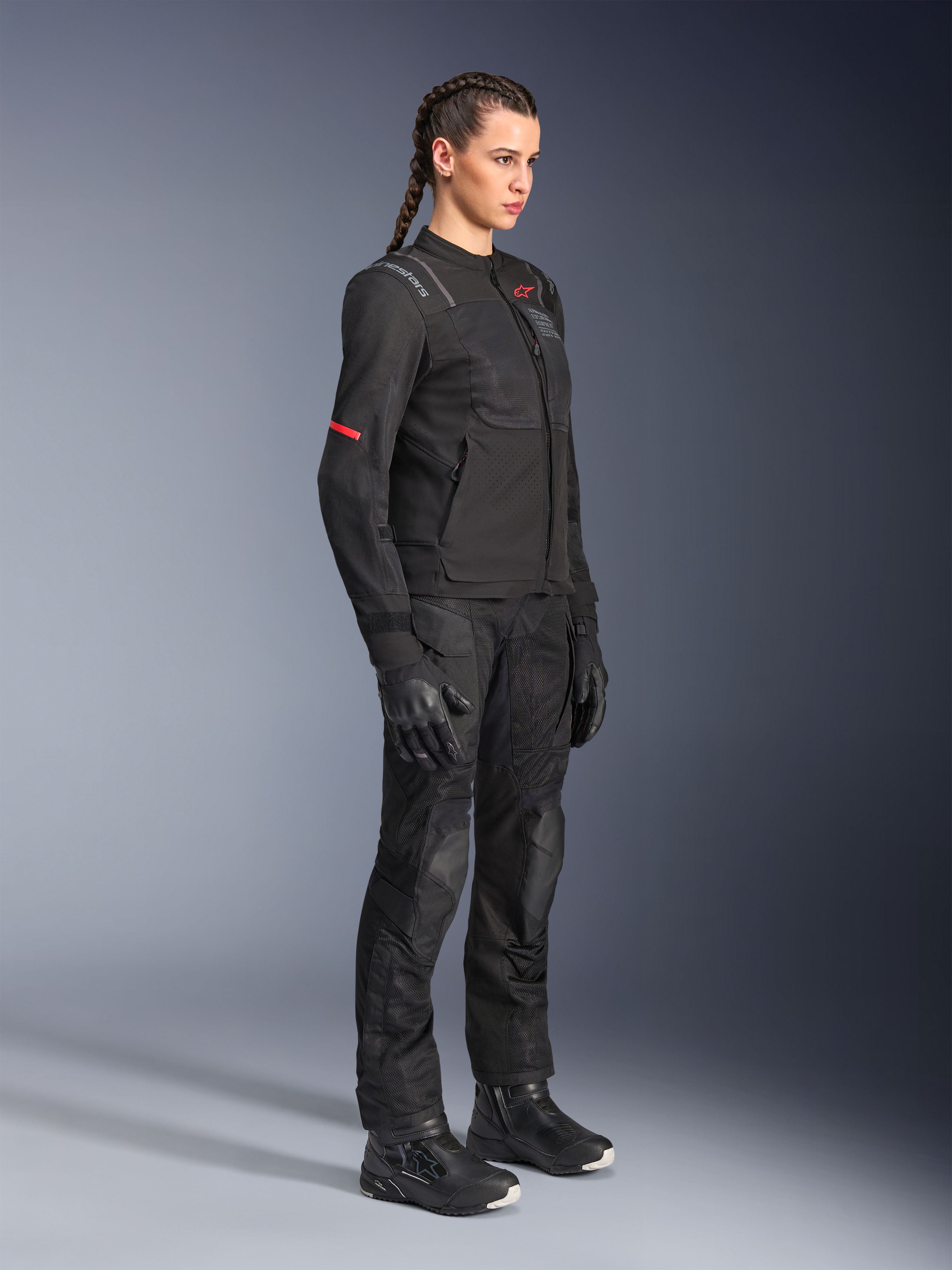 Mujer piloto vistiendo los pantalones Alpinestars Stella Andes Air Drystar® en color negro, pantalones textiles de aventura con paneles de ventilación de malla, combinados con una chaqueta Stella, guantes y botas a juego para un conjunto completo de turismo en moto.