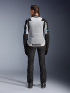 Chaqueta Alpinestars Stella ST-2 Air, Ice Gray Black, vista trasera en modelo femenina, con un gran panel de malla gris claro en la espalda, mangas negras con detalles de franjas azules, logotipo de Alpinestars en la parte inferior de la espalda, combinada con pantalones técnicos de conducción y botas negras, equipamiento de touring de verano para moto
