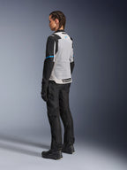 Mujer piloto con la chaqueta Alpinestars Stella ST-2 Air en Ice Gray y negro, vista trasera de tres cuartos que resalta el gran panel de malla gris claro en la espalda, mangas negras con una franja azul y el logotipo de Alpinestars en azul, combinada con pantalones, guantes y botas de moto negros para un conjunto completo de adventure touring