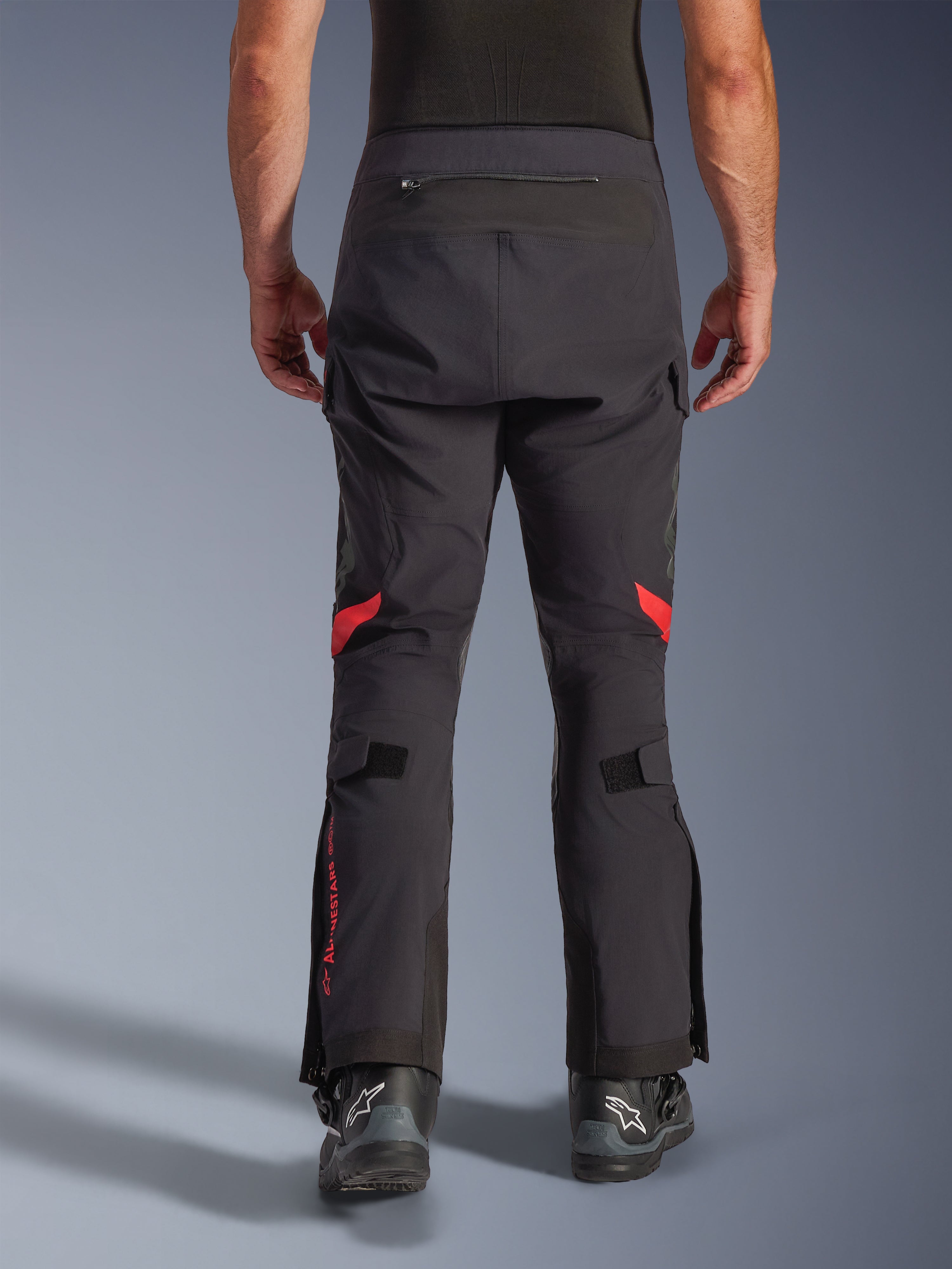 Pantalones laminados Alpinestars Halo Pro Drystar® XF, Negro Dark Shadow, vista posterior de pantalones de moto de aventura con detalles rojos detrás de las rodillas y marca roja en la pantorrilla, usados con botas negras Alpinestars, tejido laminado 3L duradero para rendimiento todoterreno