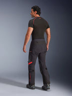 Pantalones laminados Alpinestars Halo Pro Drystar® XF, color Black Dark Shadow con detalles rojos, vista trasera en modelo masculino, combinados con una capa base negra y botas de moto, equipo técnico de aventura para conducción todoterreno