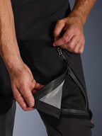 Pantalones laminados Alpinestars Halo Pro Drystar® XF, negros, primer plano de una persona abriendo la ventilación del muslo con una cremallera impermeable, revelando un forro de malla negra para ventilación directa, detalle funcional de pantalones de moto de aventura.