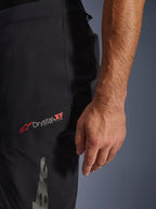 Alpinestars Halo Pro Drystar® XF Laminated Pants, color Black Dark Shadow, vista de primer plano de la parte superior de la pierna con el logotipo Drystar® XF en rojo y blanco, tejido técnico impermeable para conducción de aventura