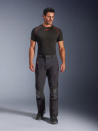 Pantalones laminados Alpinestars Halo Pro Drystar® XF en color Black Dark Shadow, usados por un modelo con una capa base negra y botas de moto, con ventilaciones técnicas con cremallera en los muslos, bolsillos cargo y paneles reforzados en las rodillas; equipamiento de motociclismo para adventure touring.