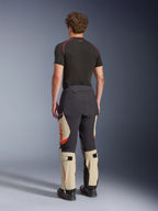 Pantalones laminados Alpinestars Halo Pro Drystar® XF, pantalones de moto de aventura, negro Mastic y tostado con detalles en naranja, vista trasera que muestra la construcción de la capa laminada de 3 capas, combinados con una capa base negra y botas de aventura.