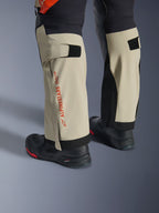 Pantalones laminados Alpinestars Halo Pro Drystar® XF, Mastic Black, primer plano de la parte inferior de las piernas con el logotipo de Alpinestars en rojo y ajustadores de velcro en la pantorrilla, usados con botas de aventura negras