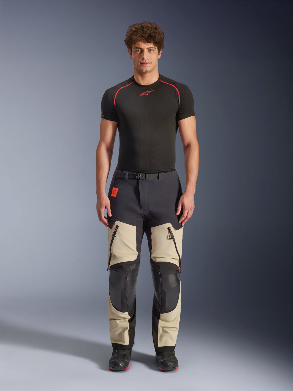 Pantalones laminados Alpinestars Halo Pro Drystar® XF, Mastic Black, pantalones de moto de aventura usados por un modelo con una capa base negra y botas, con paneles beige en los muslos con grandes ventilaciones con cremallera, secciones de rodilla reforzadas en negro y un cinturón con hebilla magnética.